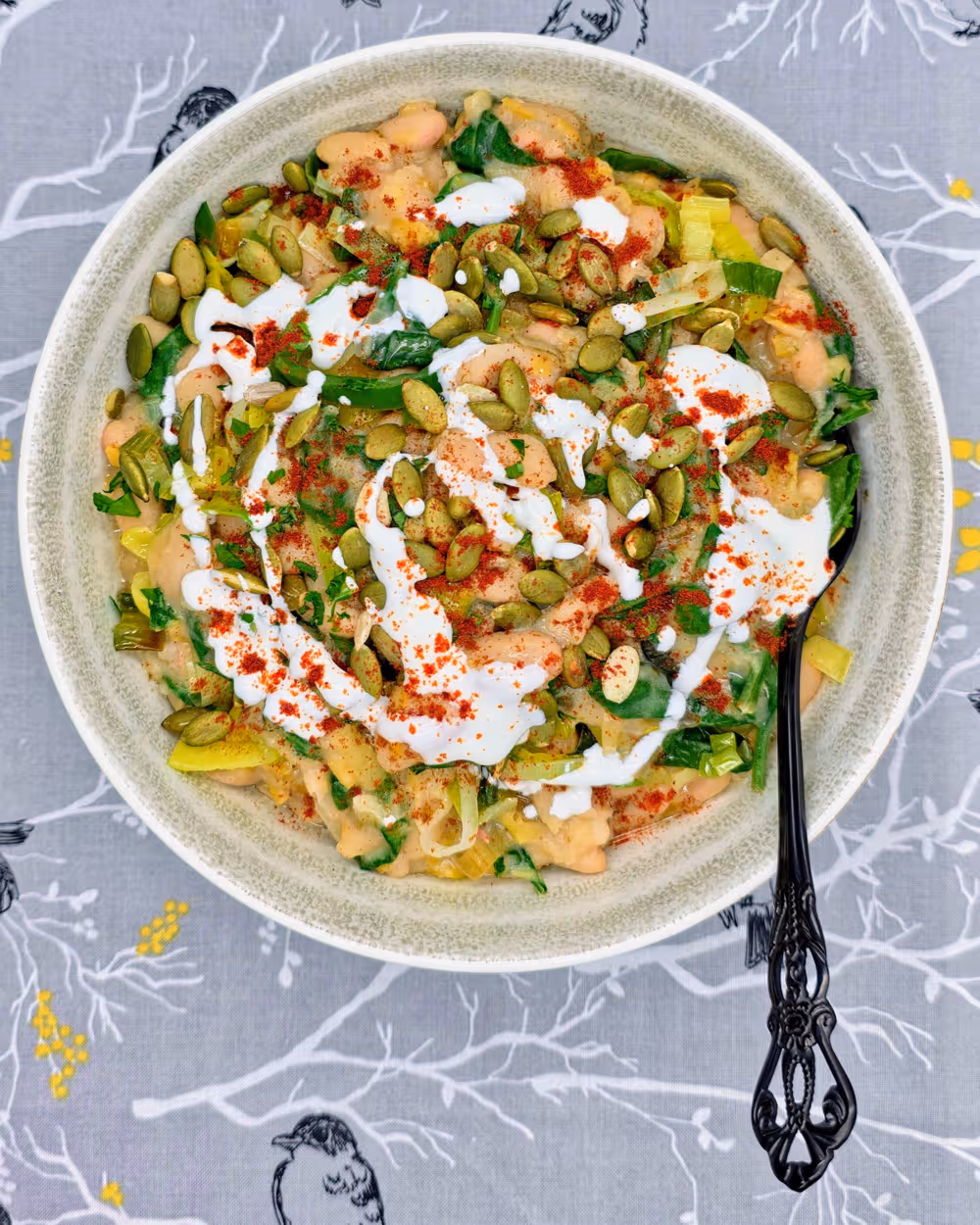 Leeky Beans plated in a bowl and topped with a sprinkle of toasted pumpkin seeds, a drizzle of Greek yoghurt and a sprinkle of smoked paprika.